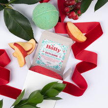Load image into Gallery viewer, An open box of Holly Bath Bomb, styled with red ribbon, green leaves, apple slices, and a green bath bomb on a white background.