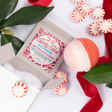 Load image into Gallery viewer, A holiday-themed bath bomb set featuring a round red-and-white bath bomb, an open kraft paper box labeled 'Candy Cane Bath Bomb', and scattered red-and-white peppermint candies on a white background with green leaves and red ribbon.