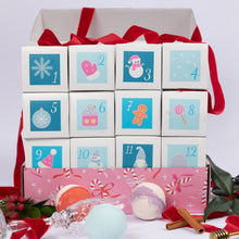 Load image into Gallery viewer, A Christmas advent box with 12 numbered gift boxes arranged in a grid, tied with red ribbons, with colorful bath bombs, cinnamon sticks, and holiday greenery in the foreground.