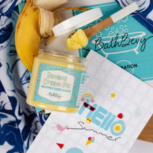 Load image into Gallery viewer, Jar of Banana Cream Pie scented soap scrub with a brush on a blue and white patterned towel.