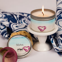 Load image into Gallery viewer, Candle with a heart design on a white stand, surrounded by a blue and white patterned fabric and a small plant.