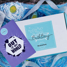 Load image into Gallery viewer, A BathBevy Relaxation subscription box in white and light blue, styled with a purple 'Out of this World' card and a silver ribbon on a blue abstract background.