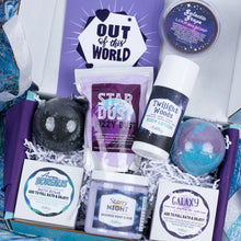 Load image into Gallery viewer, A curated bath and body gift box filled with spa products including a Starry Night whipped soap scrub jar, Twilight Woods body lotion bottle, and various bath bombs, all arranged in white paper shred inside a purple and blue box.