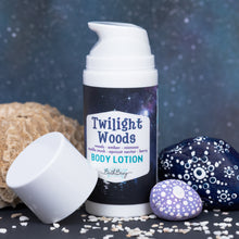 Load image into Gallery viewer, A bottle of Bath Bevy Twilight Woods Body Lotion stands upright on a dark surface, with its cap placed beside it. The bottle has a white pump and a dark label with a galaxy print and teal text.