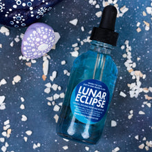 Load image into Gallery viewer, A bottle of Lunar Eclipse Crystal Infused oil, filled with vibrant blue liquid, set against a dark blue textured background scattered with white shell pieces.