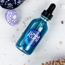 Load image into Gallery viewer, A blue glass dropper bottle labeled 'Lunar Eclipse', styled on a white wood background with decorative stones and seashells.