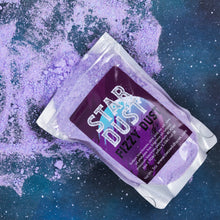 Load image into Gallery viewer, A silver pouch of Star Dust Fizzy Dust, shown diagonally on a dark blue starry background with purple powder spilled around it.