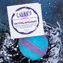 Load image into Gallery viewer, A bath bomb package labeled GALAXY  sits above a blue and purple spherical bath bomb on a dark, sparkly background. The package text reads 'LEMON RIND - GRAPEFRUIT - LILY - VANILLA SUGAR' and 'ADD TO FULL BATH &amp; ENJOY!'.