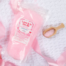 Load image into Gallery viewer, Pink bath salt package with a wooden scoop on a textured white surface with pink ribbons.